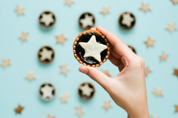 Hand holds star shaped tart on mint color background, top view