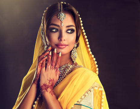 Portrait of beautiful indian girl . Young hindu woman model  with tatoo mehndi  and kundan jewelry . Traditional Indian costume  yellow saree

