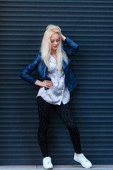 Young beautiful smiling blonde girl with beautiful appearance and long hair Smiling girl with a beautiful face and a charming look to have fun. Urban fashion style girl posing against a blue iron wall