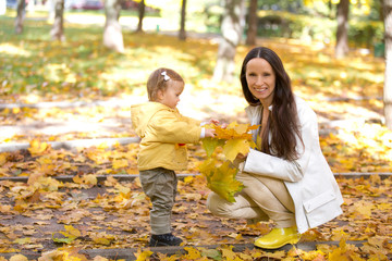 Mother and child playing with leaves in autumn park