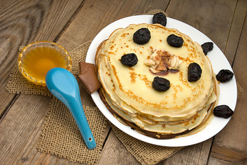 Pancakes with berries, fruits, chocolate, pine nuts and honey on white plate on a natural wooden board