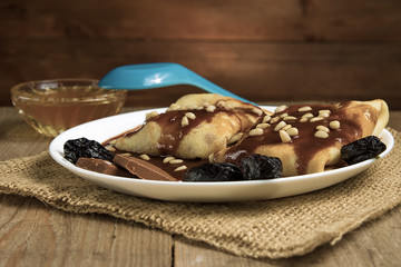 Pancakes with berries, fruits, chocolate, pine nuts and honey on white plate on a natural wooden board