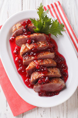 Tasty sliced roast duck breast with cranberry sauce on a plate close-up. vertical top view