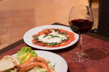 Restaurant food with fresh ingredients - tomatoes with mozzarella and fresh basil and glass of red wine