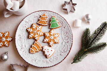 Beautiful Christmas background with gingerbread cookies on a white plate with a branch of a tree and forms for cookies