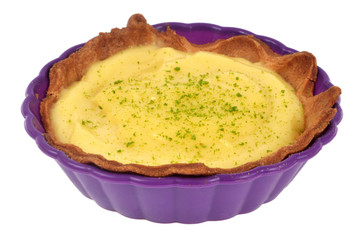Tartelette au citron avec des zestes de citron vert dans un moule en silicone sur fond blanc