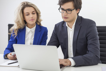 Woman in blue blazer and a guy wearing glasses are in the office