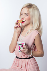 beautiful fashionable cheerful girl in a pink dress in a retro style with a croissant and a cup of tea on a white background isolated in studio