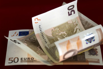 Half rolled fifty euro banknotes on fifty euro bills background on dark red. Close up image. Selective focus.