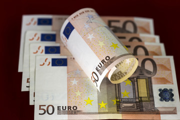 Half rolled fifty euro banknote on fifty euro bills background on dark red. Close up image. Selective focus.