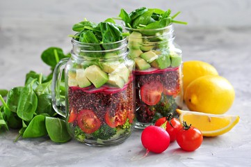Healthy salad with quinoa, avocado, tomato, red onion, baby spinach, radish and olive oil in a Mason jars.