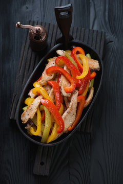 Chicken fajitas in a cast-iron pan over black wooden surface