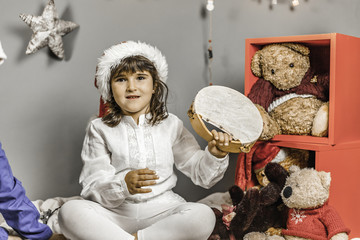 Girl wearing Santa hat and white clothes, holding a tambourine.