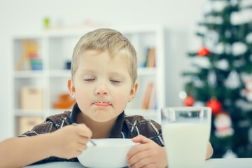 Little boy eating breakfast on the eve of the new year. Christmas tree in the background