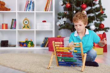 Waiting for Christmass. Cute little boy counting gifts with wooden abacus.