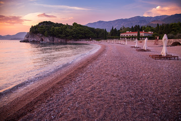 Sunbed and umbrellas on the pebble beach at sea sunset
