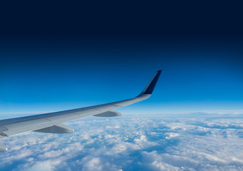 Obraz premium Wing of an airplane flying above the clouds on a clear sunny day