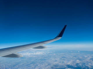 Wing of an airplane flying above the clouds on a clear sunny day