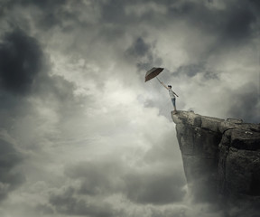 Boy trying to catch his umbrella on the edge of a cliff above the clouds. Escape and fly away.
