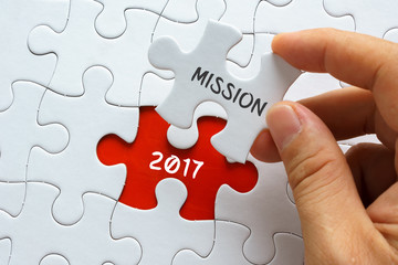 Hand holding piece of jigsaw puzzle with word MISSION 2017