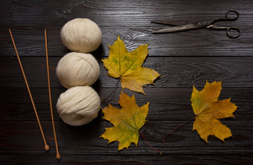 Yarn, knitting needles, scissors and yellow leaves on a table