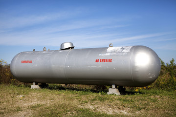 Fototapeta na wymiar Shiny silver propane tank in field under blue sky. Horizontal.
