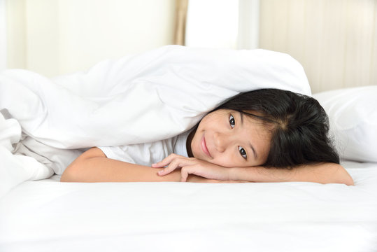 Portrait of happy young Asian girl lying on the tummy in bedroom