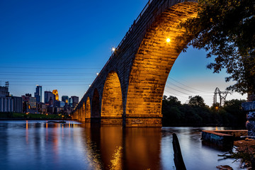 A view of the beautiful stone arch bridge of Minneapolis, MN, USA at dusk, showing part of the city skyline