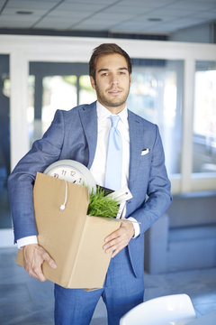 Getting fired. Shot of a young care-worn businessman holding hand a cardboard box while leave his office. 