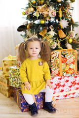 girl sitting on a box with gifts. Christmas tree in the backgrou