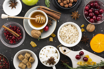 Various ingredients for winter seasonal baking and other recipes, pomegranate, honey, orezhi, apples, persimmons, herbs  spices on a dark background. Top view.