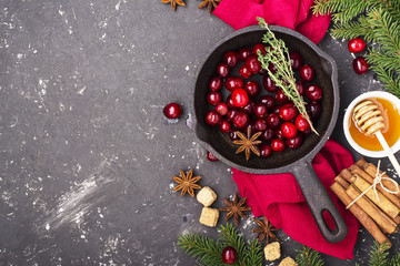 Fresh homemade cranberry sauce in a pan on dark wooden background with scattering of ripe berries.