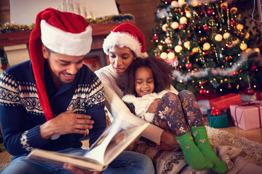 Happy family reading book at home by fireplace