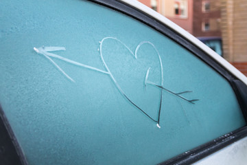 Cupid heart drawn on a frozen windscreen.
Cold as ice. Winter is coming.
Houses in the background.