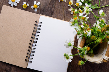 Blank notebook with white flower and bas ket of flower on vintage wooden table View from above with copy space