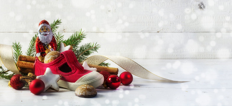 Childrens red shoe filled with sweets and christmas decoration for Nicholas day on the 6th December, white wooden background, panorama format