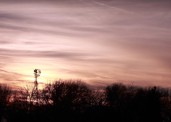 Old windmill on a farmstead with trees at sunset