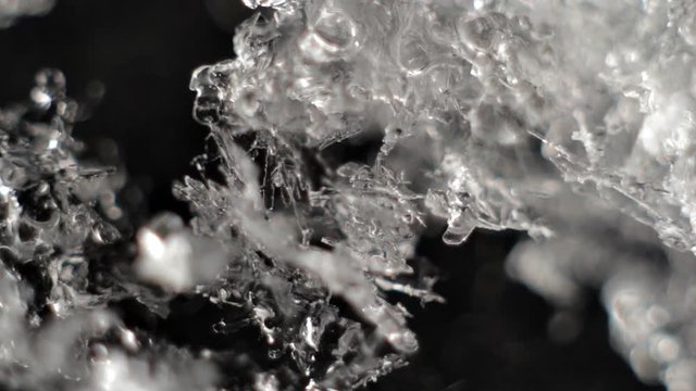 Snow Melts Macro. Snow crystals melt and turn into water on black background.
