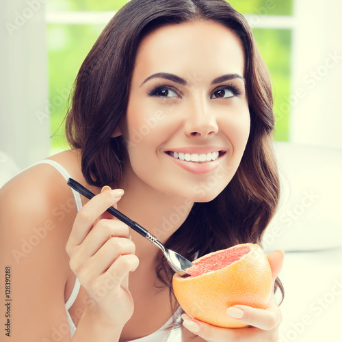 "Smiling young woman eating grapefruit at home" Stock photo and royalty