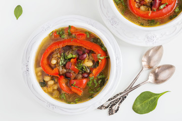 Spiced vegan kidney bean and lentil thick soup with tomatoes and bell pepper. Vintage ceramic bowl on white table, top view.