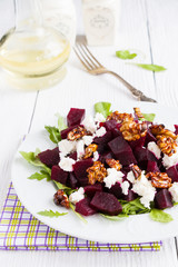 Dietary salad of beets, arugula, feta cheese and caramelized walnuts with olive oil and lemon juice. White wooden table.