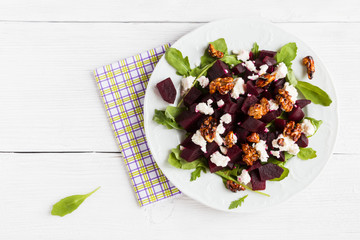 Dietary salad of beets, arugula, feta cheese and caramelized walnuts with olive oil and lemon juice. White wooden table, top view.