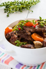 Beef Bourguignon in a white soup bowl. Stew with carrots, onions, mushrooms, bacon, garlic and bouquet garni. The dish is served with fresh thyme.