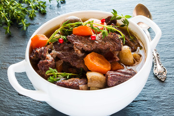 Beef Bourguignon in a white soup bowl on black stone background. Stew with carrots, onions,...