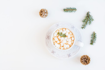 Cozy warm knitted scarf, fir branches and cacao with marshmallows in vintage cup with saucer.  White table, top view, flat lay.