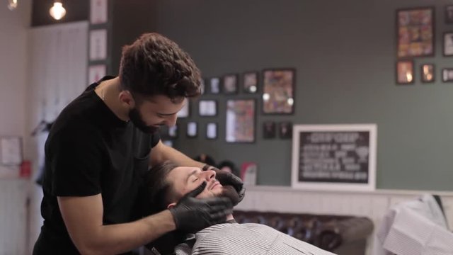 Barber combing beard of client and dancing at a barber shop.