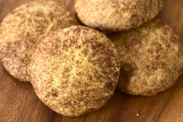 Homemade snickerdoodle cookies with cinnamon and sugar coating on wooden plate, photographed with natural light (Selective Focus, Focus in the middle of the cookie in the front)
