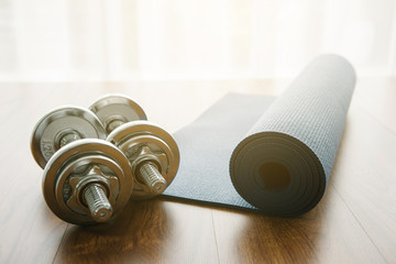 Silhouette Pair of dumbbells with blue yoga mat on wood floor,flare light - Powered by Adobe