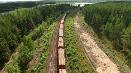 Obraz premium Cars of freight train passing to a distance at the double line railway in forests of Karelia, Russia. Aerial rear view