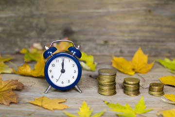 Alarm clock and money coins on wooden rustic old table with autu
